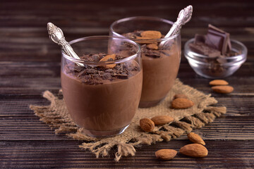 Chocolate mousse with almonds in glasses on a dark wooden background.	