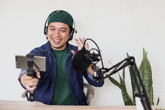Asian young man in casual style make a vlog using smartphone on podcasting room, say hi to the camera.