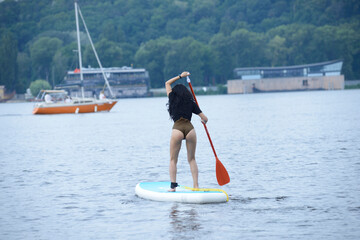 Naklejka premium Young woman in a swimsuit rowing a SUP board on the river