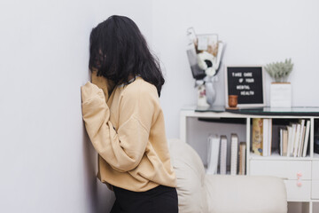 Young Asian woman is standing and burying her face to the wall, feeling depressed. Millennial lady having mental problems or mood disorder.
