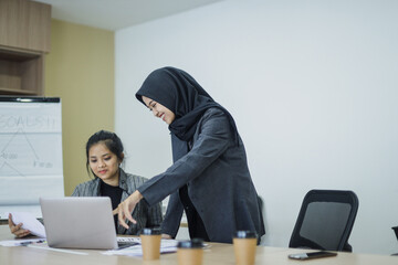 Confident businesswoman pointing at laptop screen, training and mentoring new employee, working together at the office.