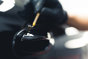 Professional car detailing. Closeup indoor portrait of expert mechanic using small brush to touch up door handle. High quality photo