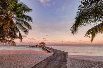 Amazing sunset landscape. Picturesque summer sunset in Maldives. Luxury resort villas pier path seascape with soft led lights under colorful sky palms. Dream sunset tropical sea shore fantastic nature