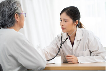 Young female medical doctor examining senior woman patient in hospital. Asian elderly visit professional physician to examine her health. Young nurse friendly talking to sick patient for medicine.