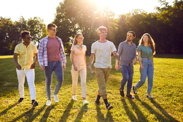 Diverse group of friends hanging out and spending time outside. Six happy young multiethnic people enjoying good weather on beautiful summer day, walking in green park, and having fun together