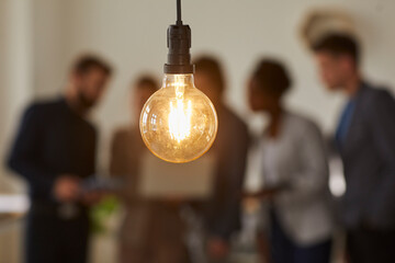 Glowing light bulb and business people over blurred background. Hanging light bulb on foreground,...