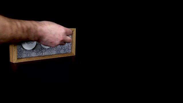A wooden calendar block showing the date February 25th with a mans hand putting on and taking off the metal discs with the date and month on them, filmed in 4k quality