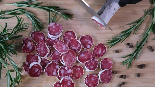 Traditional Spanish Fuet thin dried sausage. Closeup of cutting sausage fuet from pork meat on a table at a kitchen. Slices of red Spanish dry sausage fuet