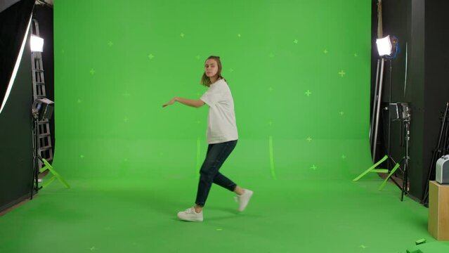 A young woman dancing on a green screen background. Attractive girl making content for social media. Modern female video blogger having fun. Chroma key