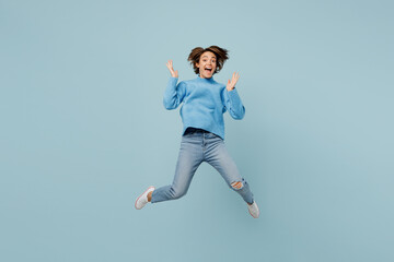 Full body overjoyed exultant excited young woman wear knitted sweater look camera jump high spread hands isolated on plain pastel light blue cyan background studio portrait People lifestyle concept.