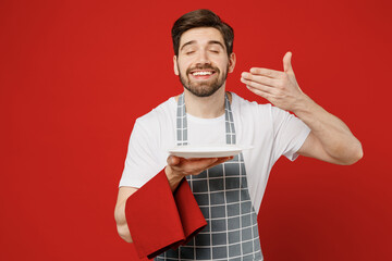 Young waiter male housekeeper chef cook baker man wear grey apron towel hold empty plate with area...