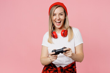 Young excited smiling happy woman wear white t-shirt red hat hold in hand play pc game with joystick console isolated on plain pastel light pink background studio portrait. People lifestyle concept. © ViDi Studio