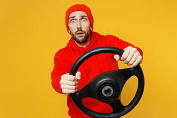 Young shocked confused surprised sad caucasian man wear red hoody hat look camera hold steering...