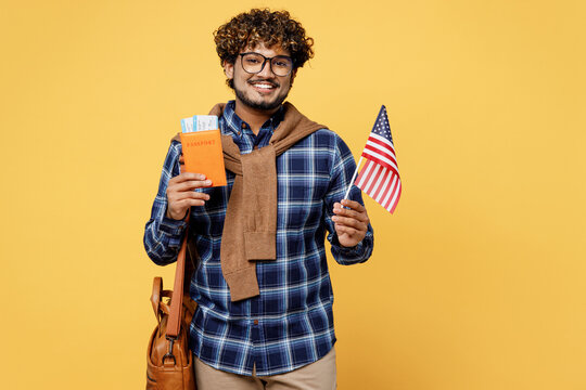 Traveler teen Indian boy IT student wear casual clothes hold passport ticket American flag isolated on plain yellow background Tourist travel abroad in free time rest getaway. Air flight trip concept.