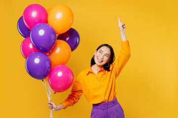 Fototapeta na wymiar Happy fun young cool woman wears casual clothes celebrating hold bunch of colorful air balloons point index finger up on area isolated on plain yellow background. Birthday 8 14 holiday party concept.