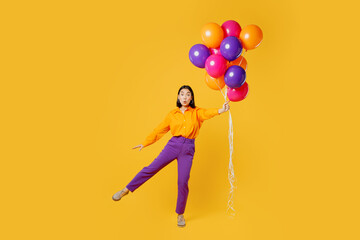 Fototapeta na wymiar Full body shocked surprised happy fun young woman wearing casual clothes hat celebrating hold bunch of balloons raise up leg isolated on plain yellow background. Birthday 8 14 holiday party concept.