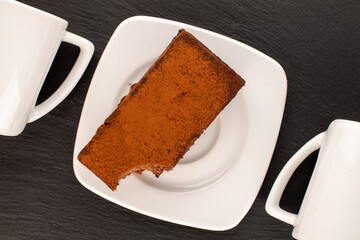 One piece of truffle cake with ceramic white saucer and two cups on slate stone, macro, top view.