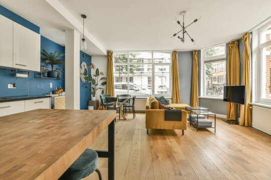 a living room with wood flooring and blue accent on the wall behind it is an open kitchen, dining area