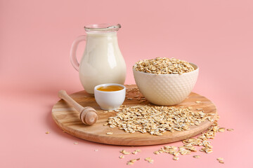 Wooden board with bowl of raw oatmeal, milk and honey on pink background