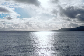 Sun beam reflection in the ocean . Low clouds over the island