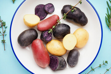 Plate with raw potatoes and herbs on color background, closeup