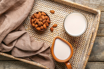 Tray with jug, glass of healthy almond milk and nuts on wooden table, closeup