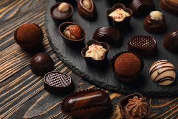 Slate board with chocolate candies on wooden background, closeup