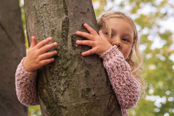 Blond girl child embracing with two hands a tree in the park