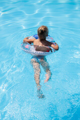 Child girl swims with an inflatable ring in a summer pool. Top view, flat lay
