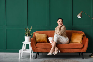 Young woman sitting on red sofa near green wall