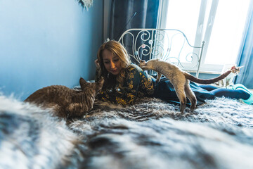 Woman spending time with Devon Rex cats on a bed. High quality photo