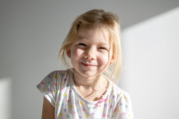Beautiful smiling child girl blonde on the background of a white wall.