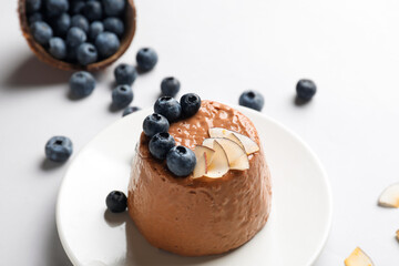 Plate with delicious chocolate pudding, coconut slices and blueberry on white background