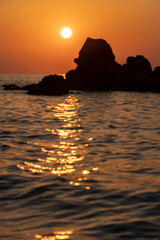 Blurred defocused ocean seascape with rocks. Blurry orange and golden skylight calmness relaxing summer mood. Sunset sky reflecting in the water Travel destination, vacations concept.