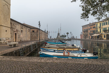 Fototapeta na wymiar Old harbor of the small and picturesque town of Lazise on Lake Garda in the winter season. Lazise, Verona province, northern Italy - January 21, 2022
