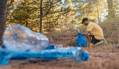 Hombre voluntario forestal, recogiendo basura de la naturaleza, con las botellas en primer plano desenfocadas.