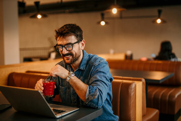 Portrait of a journalist stylish guy writing a story in a workplace in loft styled coworking, casually dressed in a denim shirt, sitting alone.