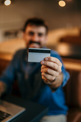 Man using a credit card and laptop for online shopping and paying. Focus on the credit card.