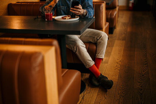 Man in a casual cool outfit sitting in a restaurant, drinking a smoothie, eating a club sandwich, and checking his social media.
