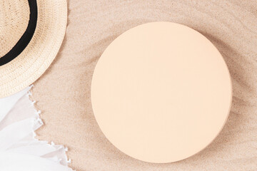 Empty beige round platform podium mockup for beauty cosmetics or products presentation. Straw hat and white crumpled linen fabric cloth on natural white beach sand background. Top view