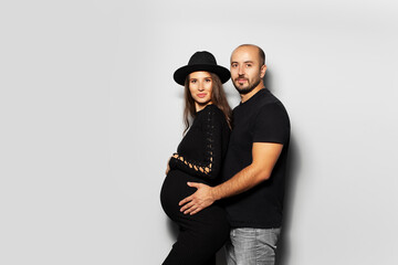 Fototapeta premium Studio portrait of young couple, future parents. Husband hugging a his wife, on white background. Wearing black.