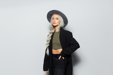 Studio portrait of young beautiful blonde girl with a braid, wearing black coat and grey hat, on...
