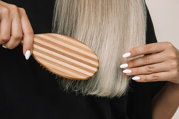 Cropped shot of a young blonde woman combing her dry straight hair with a wooden comb on a black...