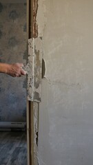 a hand with a wide spatula applies a thick mortar to the gap between the wall and the doorway, covering the wall surface after installing the door frame with putty on a trowel