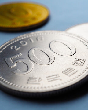 Translation: Bank of Korea. Korean coins lie on blue paper surface. 500 won coin closeup. Vertical stories illustration about economy, finance or bank. Money and business in South Korea. Macro
