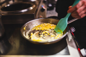 man chef cooking scrambled eggs in frying pan on kitchen