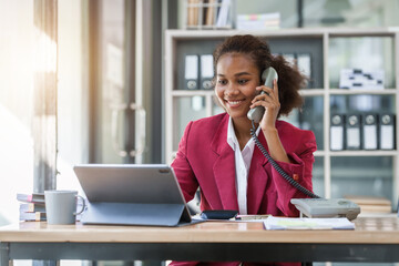 Young african american businesswoman red suit working at desk and using mobile smartphone in the modern office. Call a phone, operator.