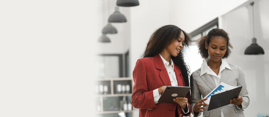 Young diverse african american female coworkers working together on start up project. Business people meeting around a boardroom table discussing creative concept, holding tablet