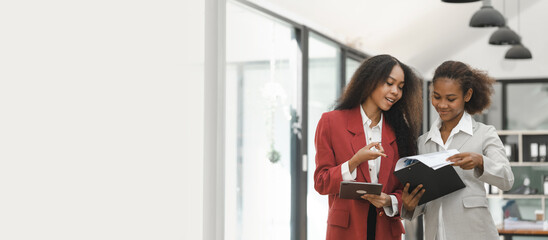 Young diverse african american female coworkers working together on start up project. Business people meeting around a boardroom table discussing creative concept, holding tablet