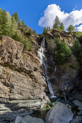 Fototapeta na wymiar Water of Lillaz waterfall (Cascate di Lillaz) falling over granite rocks forms small karst pool under blue sky, Cogne, Aosta valley, Italy